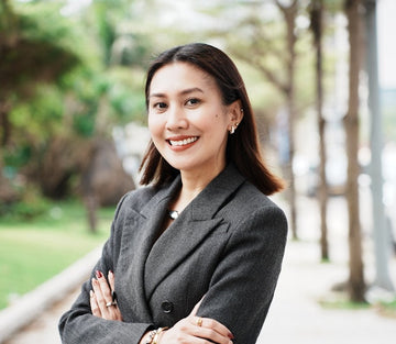 Woman in a gray suit standing outdoors with trees and greenery in the background